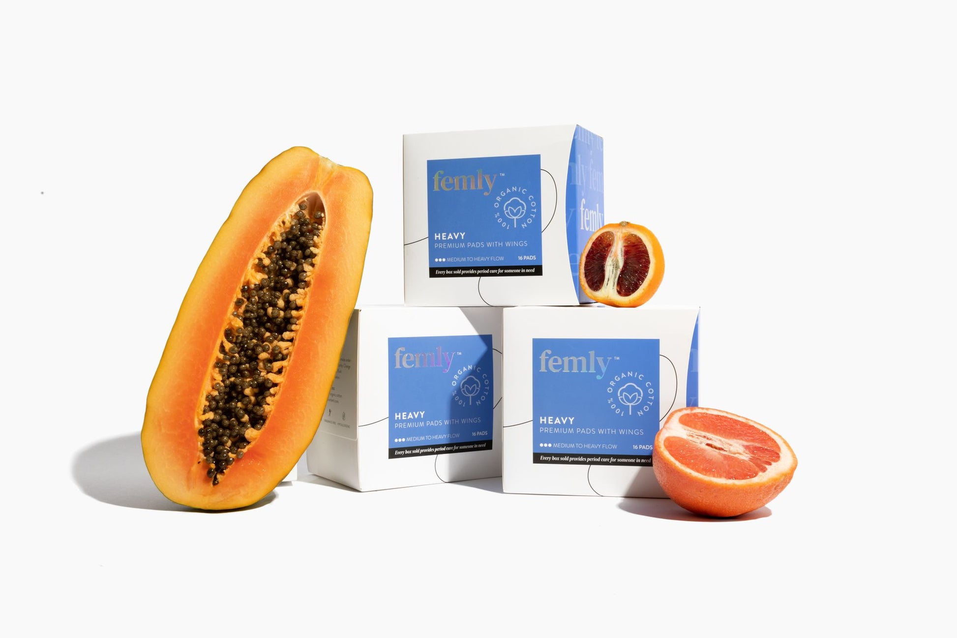 Three boxes of 100% organic cotton heavy menstrual pads surrounded by fresh fruit.